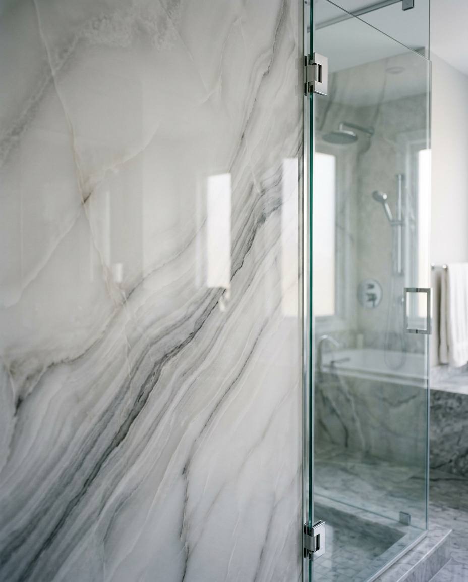Spotless seamless polished onyx shower wall panel with a frameless glass edge and no grout lines