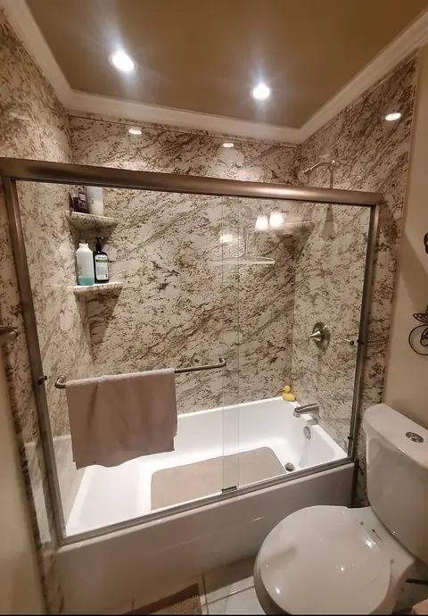 Granite-Look Tub Surround — warm granite-look tub surround with corner shelves, brushed nickel trim and a bypass glass door over a soaking tub, installed by Revive Bath Solutions in Lindale, TX